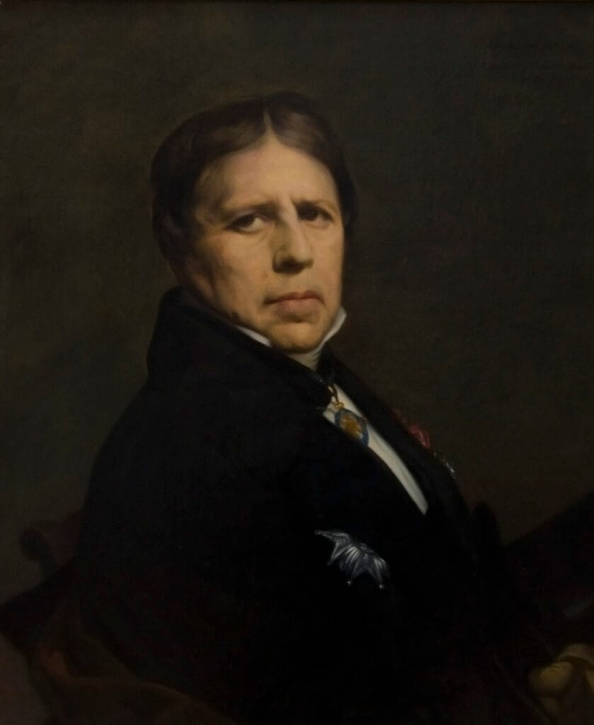 Portrait of a stern-looking person in dark, formal attire against a muted background. The subject's gaze is intense, conveying seriousness.