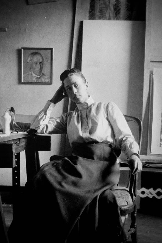 Hilma af Klint . A woman seated in a chair, reading a book placed on a table in front of her.