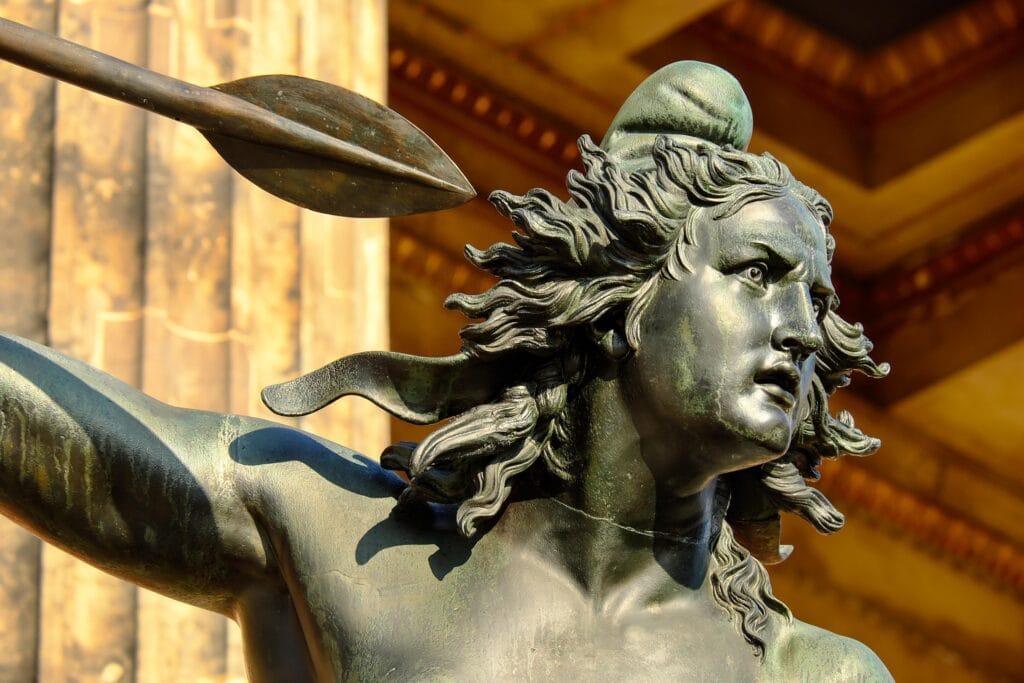 museum visit. A close-up shot of a bronze statue’s head featuring an intense facial expression and flowing hair, with a spear tip visible in the upper left.