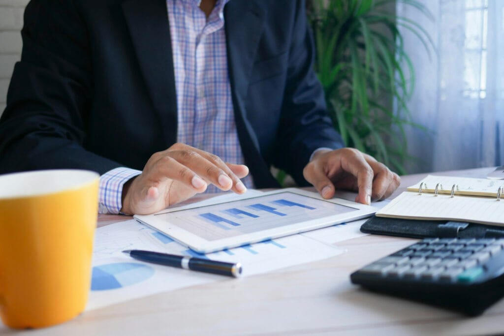 Professional reviewing financial charts on a tablet at a desk with documents and calculator.